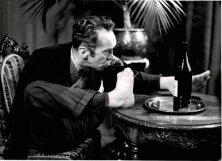 Press photograph of Charles Pasche drinking a glass of red wine with is foot