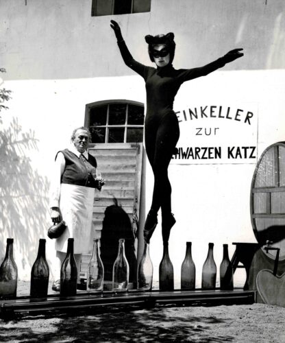 Three press photographs of a lady in a black cat suit walking on glass bottles