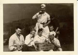 Black and white photograph of 7 people posing around a Artois crate.